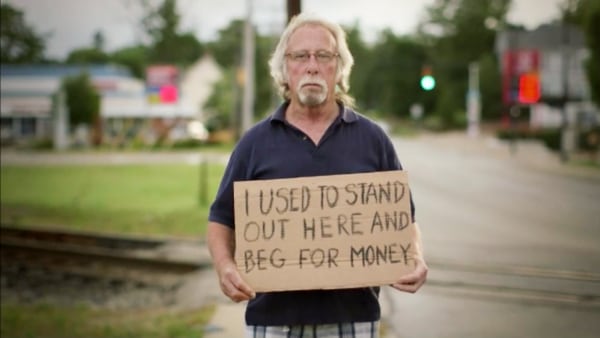 Formerly homeless man holds sign "I used to stand here and beg for money"